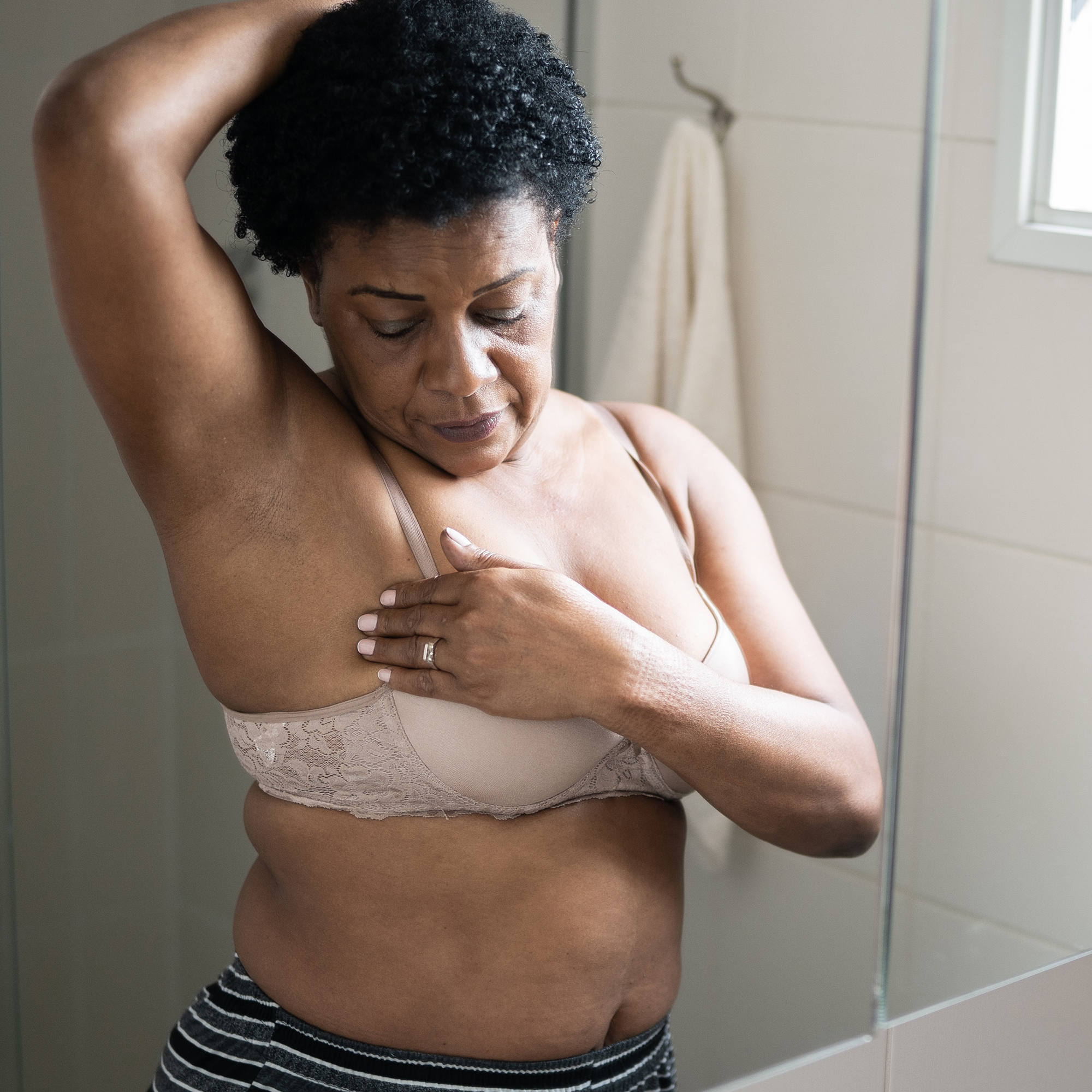 一名女子在浴室镜子前检查她的腋窝。