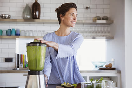 微笑的女人在搅拌机里做绿色的冰沙。