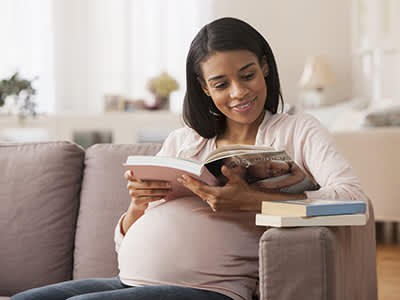 孕妇阅读沙发上，一个婴儿的书。