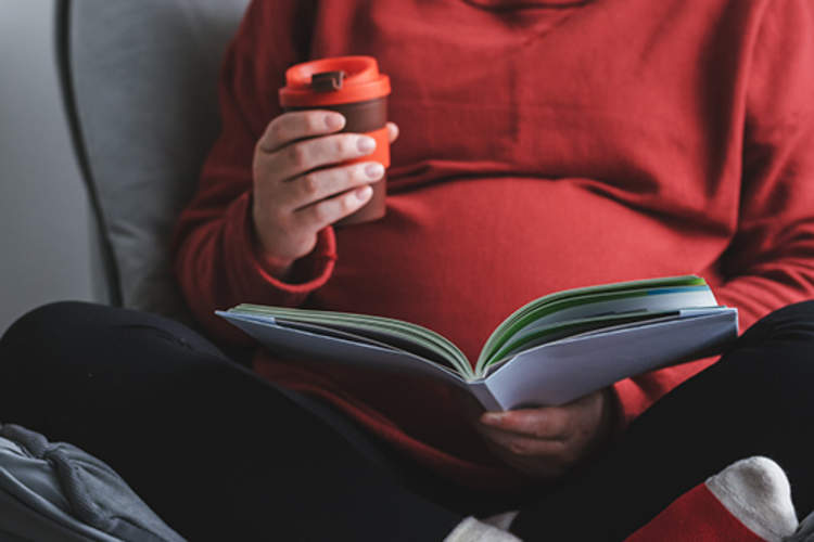 孕妇阅读手里拿着饮料。