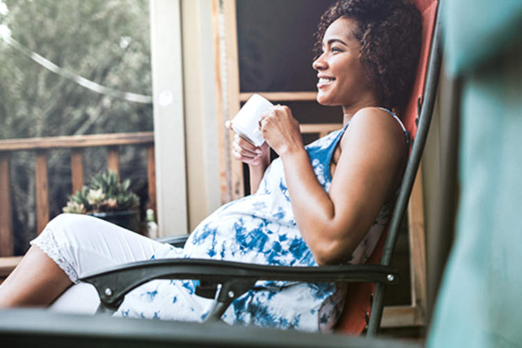 孕妇在她的门廊喝一杯茶。