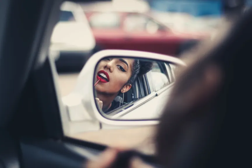 穿上在汽车后视镜的唇膏的妇女