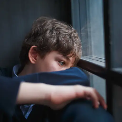 坐在窗口的一件蓝色衬衣和牛仔裤的沉思哀伤的男孩少年“loading=