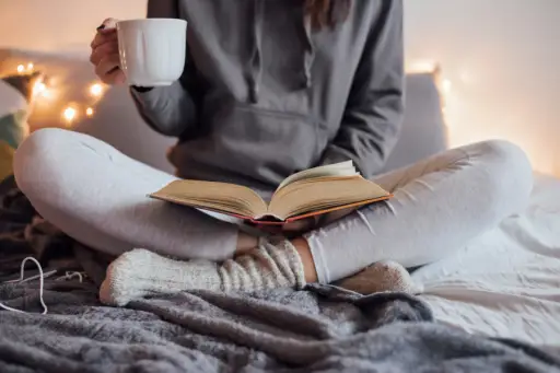 女人在床上看书，端着一杯热茶