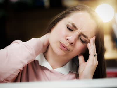 在工作中的女人头痛和颈部僵硬畏缩。