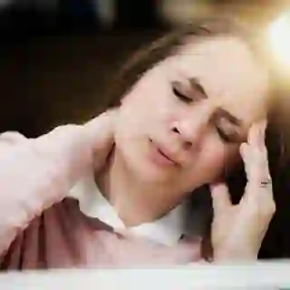Woman at work wincing from headache and stiff neck.
