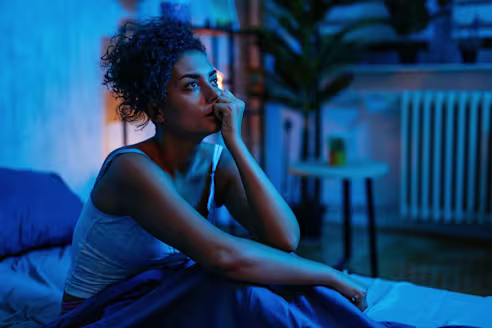 A woman sits up in bed at night