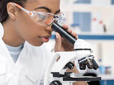 Scientist in lab coat working with microscope.
