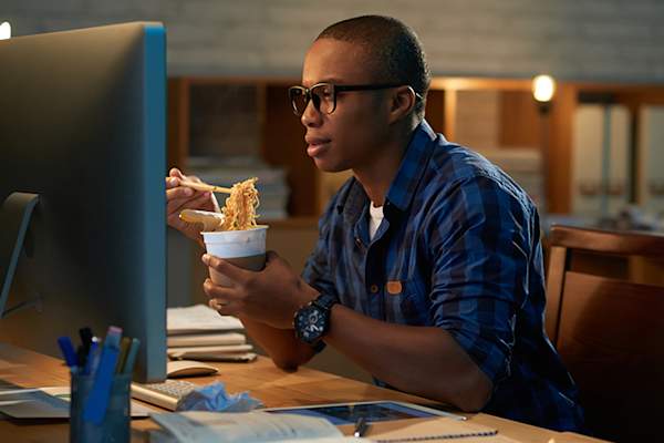 男子在晚上吃方便面在电脑前。