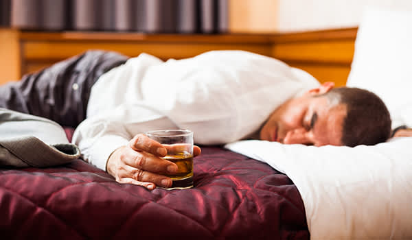 在床上拿着一杯威士忌男子睡着了面朝下。