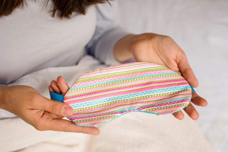 女子抱着五颜六色的睡眠面膜在床上。