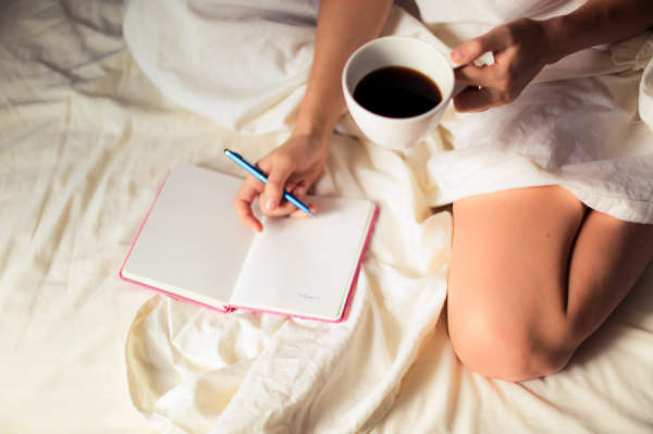女人在床上写日记，拿着咖啡