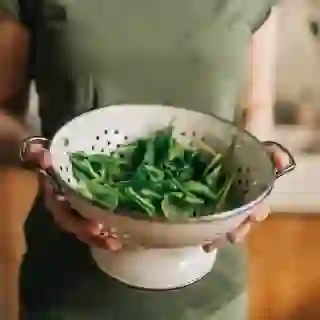 A woman holds a colander full of spinach
