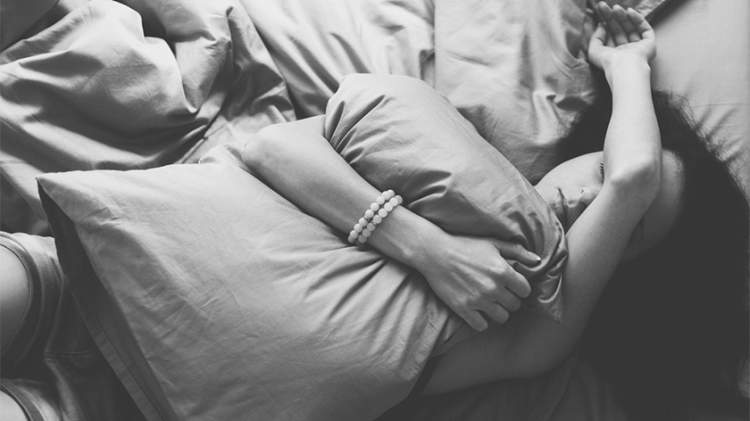 忧郁的女人的黑白照片，抱着一个枕头躺在地上。