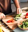Woman cutting fresh vegetables on cutting board.