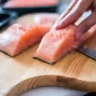 hand slicing raw salmon on cutting board