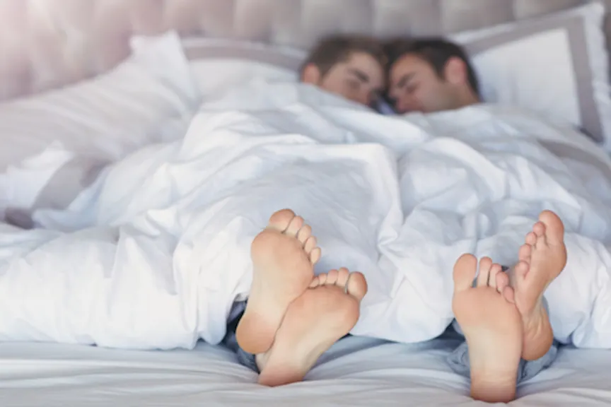 Couples feet sticking out from under covers in bed.