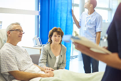 男病人在医院的病床上跟一个医生与他的妻子坐在他。