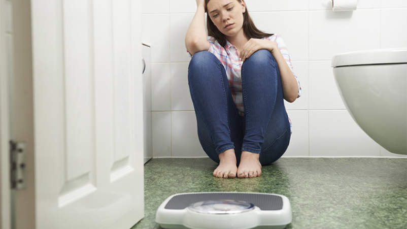 女孩青少年的饮食失调坐在浴室地板上规模。