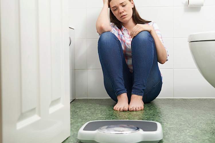 一个患有饮食失调症的少女坐在浴室的地板上。