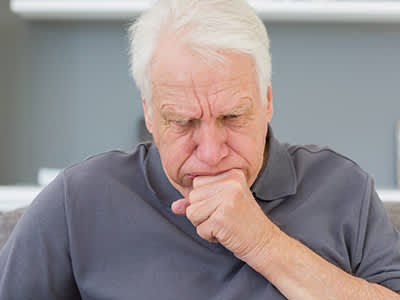 一个老人坐在沙发上咳嗽。