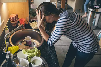 Fatigued woman struggling to clean dishes.