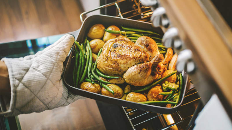 把烤鸡和蔬菜的健康晚餐从烤箱拿出来。