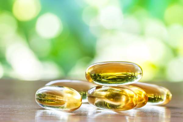 Fish oil supplement capsules on wooden table with green natural background