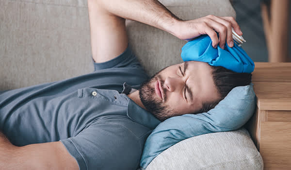 男子躺在头痛抱着他的头冰袋沙发上。