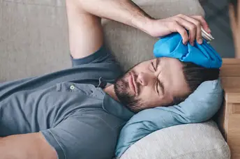 一个头痛的男人躺在沙发上，头上拿着冰袋。