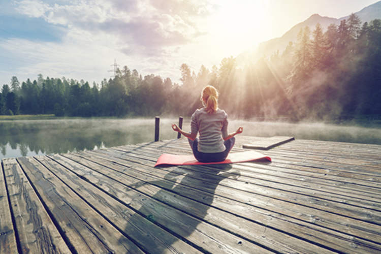 在山上湖边的码头上冥想的女人。
