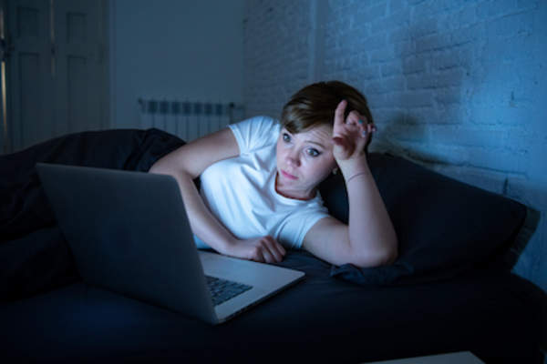 一个疲惫的女人躺在床上,手里拿着电脑。