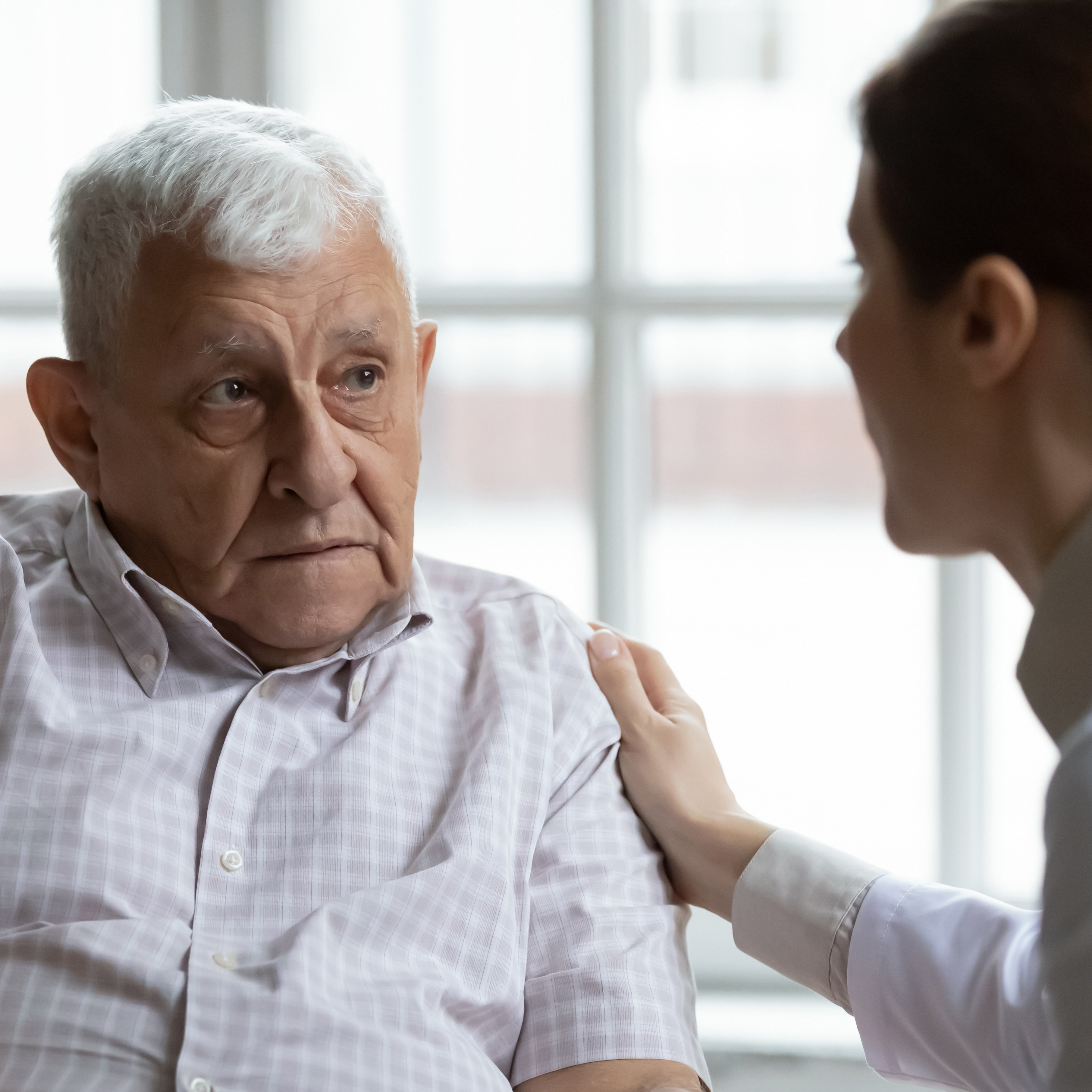 一位女医生抚摸着她的病人的肩膀，病人是一位老人，脸上带着关切的表情。