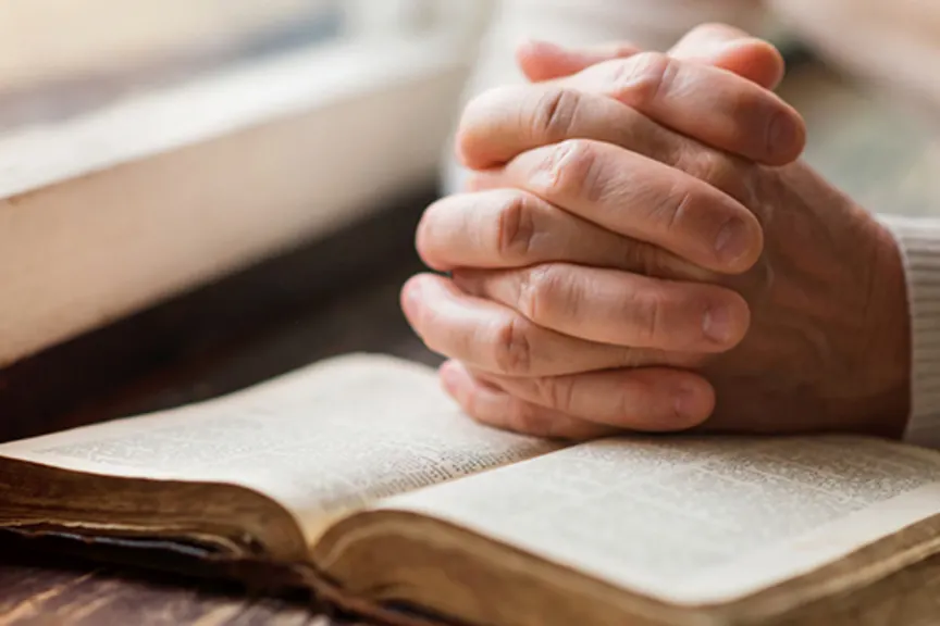 Hands clasped over religious text.