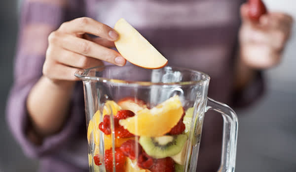 女人加入水果搅拌机制作冰沙。