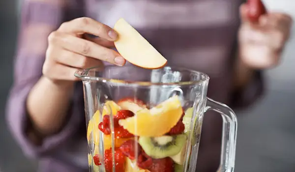 一个女人在往搅拌机里加水果做奶昔。