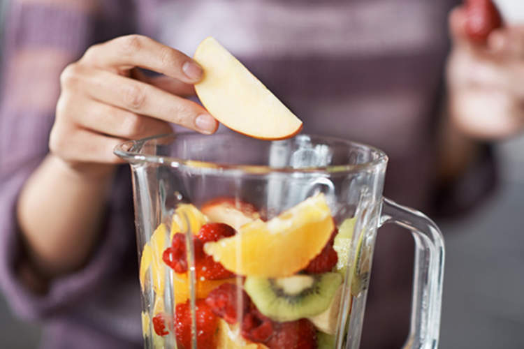 女人加入水果搅拌机制作冰沙。