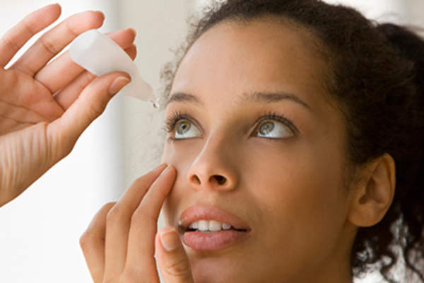 Young woman putting drops in dry eyes.