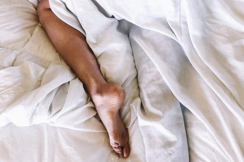 女人的腿在床上盖着被子睡觉。