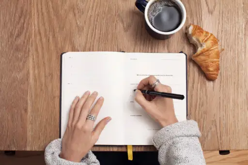 在日记中写作，咖啡和羊角面包旁边的手