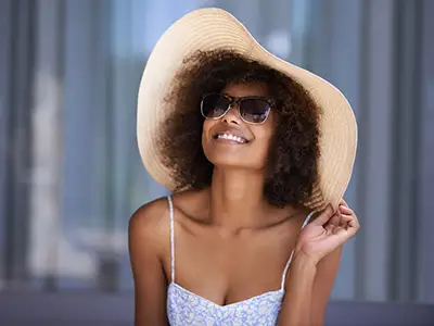 微笑的妇女佩带的太阳镜和太阳帽子。