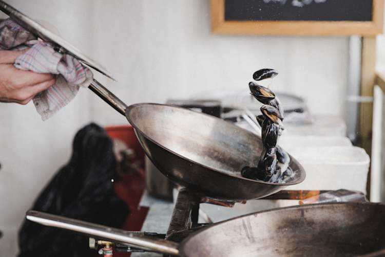 person cooking mussels in a pan