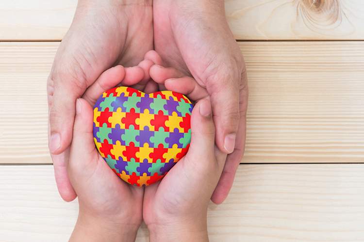 成人和儿童持有自闭症意识彩色心形拼图。