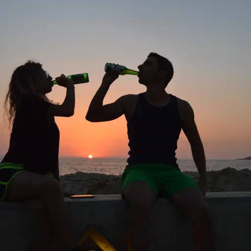 在海滩的夫妇饮用的啤酒在日落