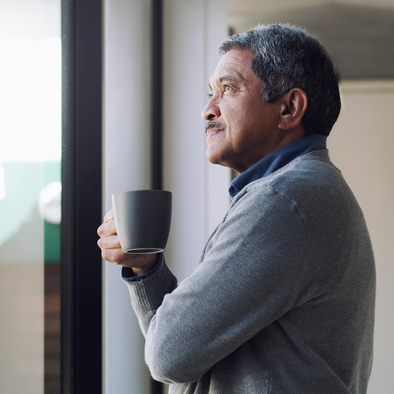 一个男人端着一杯茶看着窗外