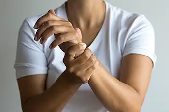 A woman holds her wrist with RA joint pain.