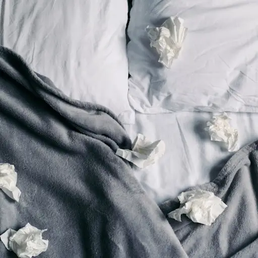 Many used tissues in an unmade bed