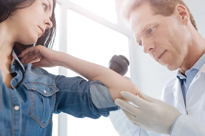 Scrupulous senior doctor using dermatoscope for skin examination.