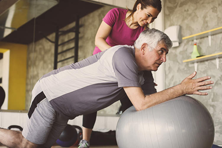 私人教练帮助高级男子在普拉提球。