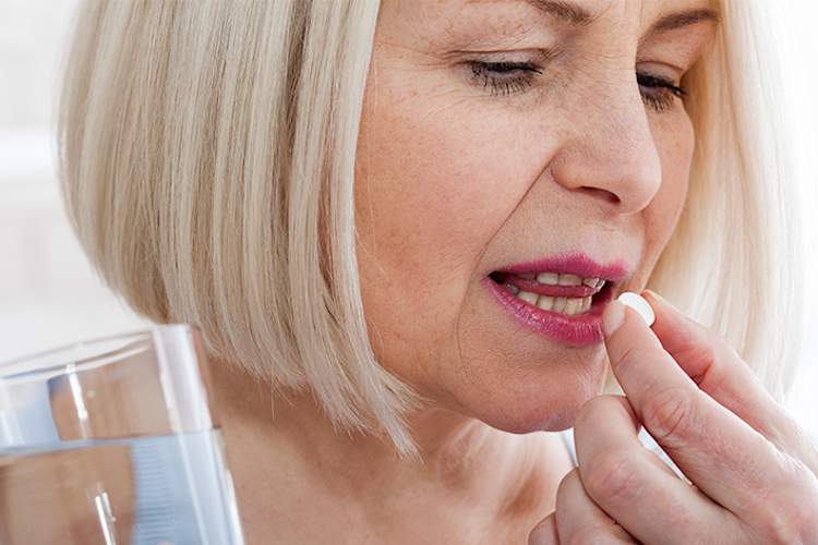 一名妇女正在服用一粒药丸和一杯水。